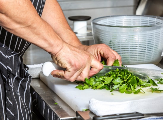 Hands chop bright green cilantro on a cutting board.